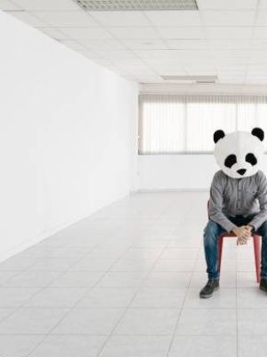 Man wearing a panda mask while sitting on a chair in an empty modern apartment.